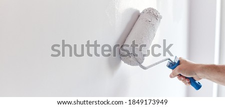 Male hand painting wall with paint roller. Painting apartment, renovating with white color paint Royalty-Free Stock Photo #1849173949