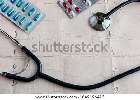 medical statoscope and tablets of different colors in blisters on a table with a cardiologist lies on a cardiogram