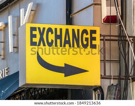 Yellow exchange sign board with a black arrow pointing in the direction of the store.