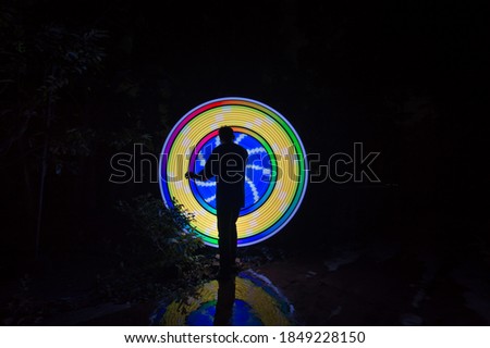 One person standing alone against a yellow and blue circle light painting as the backdrop