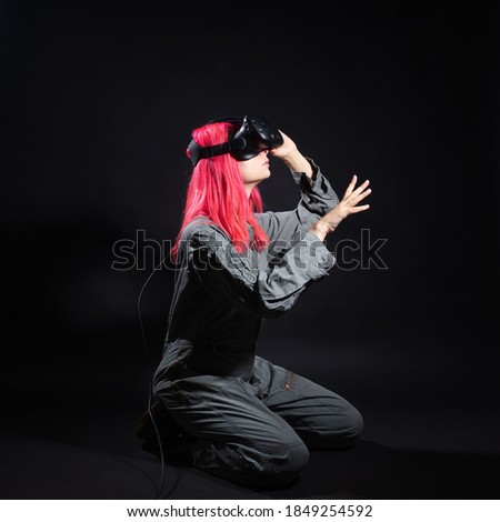 Virtual reality and futurism. Cyber punk concept, a gamer with pink hair. Young woman in overalls and virtual reality glasses, is in a simulation, black background