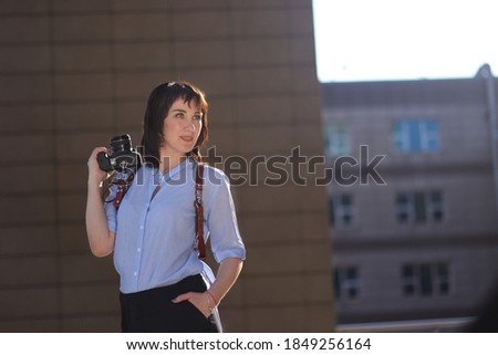 space for text modern photographer happy girl in a leather cut for the camera against the backdrop of skyscrapers. woman wearing a blue shirt, black shorts and white trendy sneakers space for text