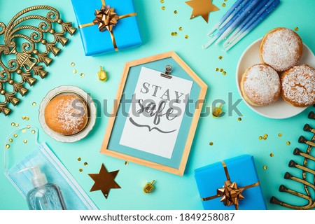 Jewish holiday Hanukkah concept with photo frame, menorah, sufganiyah and gift box over blue background. Medical face mask and sanitizer gel for coronavirus protection