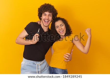 Young couple with car key celebrating on yellow background