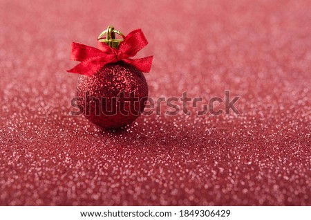 Red Christmas ball with a bow on a shiny red surface. New Year decoration.