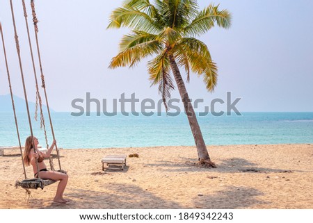 woman in a swimsuit swinging on a swing by the ocean under palm trees, sea vacation and travel.