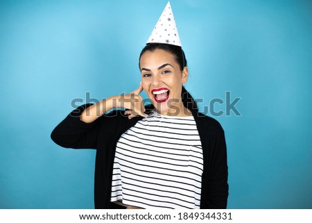 Young beautiful woman wearing a birthday hat over insolated blue background smiling doing phone gesture with hand and fingers like talking on the telephone
