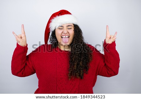 Young beautiful woman wearing a Santa hat over white background shouting with crazy expression doing rock symbol with hands up