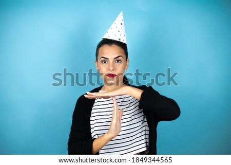 Young beautiful woman wearing a birthday hat over insolated blue background Doing time out gesture with hands, frustrated and serious face