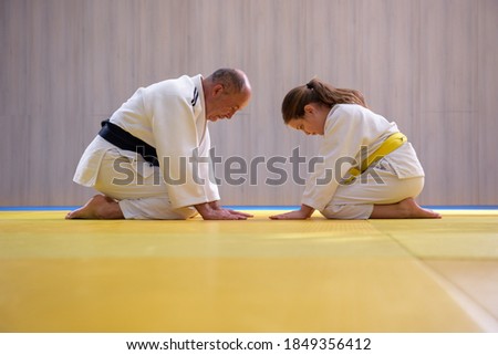 Old Judo master and young female student kneeling and bowing to each other Royalty-Free Stock Photo #1849356412