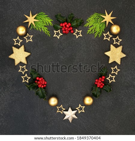 Heart shaped festive Christmas wreath decoration with holly, cedar cypress & gold star decorations on grey grunge background,. Abstract xmas composition for the holiday season.