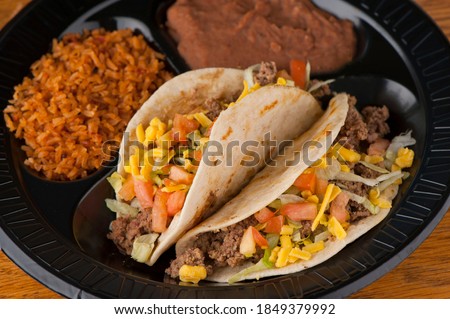 Tacos. Crispy flour and corn tortillas filled with sausage, bacon, beef, cheese, sour cream, salsa and guacamole and served with rice and beans. Classic Tex-Mex or Mexican restaurant entrée favorite. Royalty-Free Stock Photo #1849379992