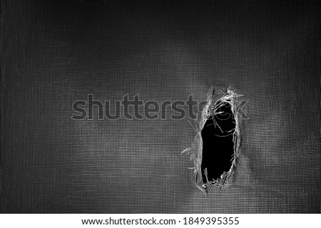 Window screen torn with a big hole against a black background.