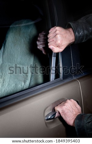 A car thief uses a Slim Jim tool to pop the lock on a car door to steal it. Royalty-Free Stock Photo #1849395403