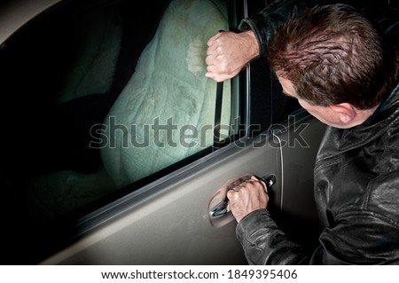 A male car thief uses a flat metal lock pick to break into a vehicle. Royalty-Free Stock Photo #1849395406