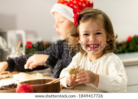 Little cute girl 2-4 with a red bow and boy 7-10 in a Christmas cap make gingerbread cookies in the New Year's kitchen.
