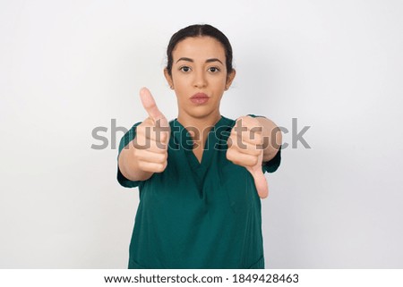 Young arab doctor surgeon woman over isolated white background showing thumbs up and thumbs down, difficult choose concept 