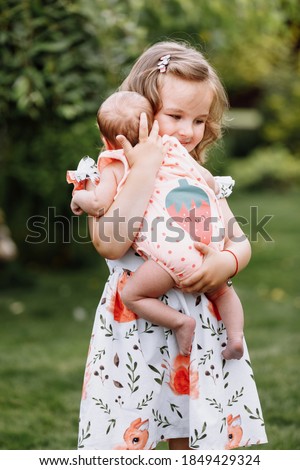 Little cute girl is holding a newborn sister in her arms and spending happy time with her outdoors