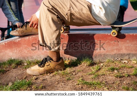 a teenager sits on a skateboard and ties his shoelaces on sneakers.