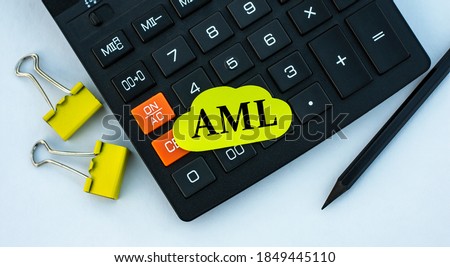 AML (Anti-Money Laundering) - word on yellow note paper on the calculator. On a white background are stationery clips with a pencil. Business and finance concept
