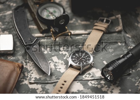Close up black dial military style wristwatch with biege nylon watch band. Wristwatch for men with military objects in the background.