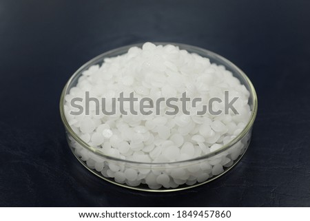 Selective focus of sodium or potassium hydroxide white chemical compound pellets or prills in a petri dish in black background. Royalty-Free Stock Photo #1849457860