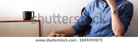 Caucasian and stylish adult man enjoying a hot cup of coffee in a cozy apartment while working from home