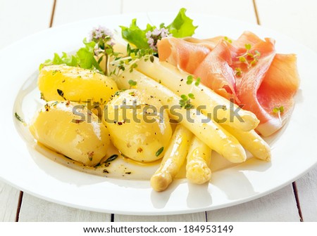Cold asparagus spears with parma ham and boiled baby potatoes served with lettuce and chopped fresh herbs, close up view on a plate