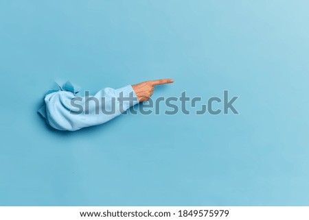 Womans hand in blue sweater breaking through paper wall demonstrates copy space for your promotional content or discount. Advertisement and proposal concept. Background texture. Banner for sales Royalty-Free Stock Photo #1849575979