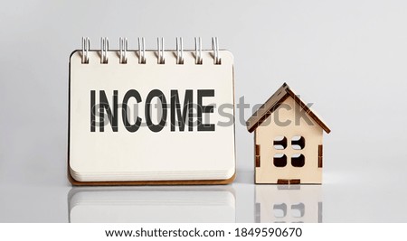 INCOME words written in an office notebook with wooden house. Financial Business