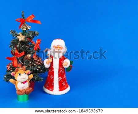 Soft toy bull, doll Santa Claus are at the Christmas tree with a bag of gifts. Isolate on a blue background. Bull as a symbol of the new year 2021. Happy New Year. Copy space. Template