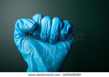 Fist in blue medical glove on the dark background.
