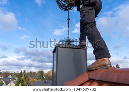 Chimney sweep cleaning a chimney standing on the house roof, lowering equipment down the flue Royalty-Free Stock Photo #1849609732