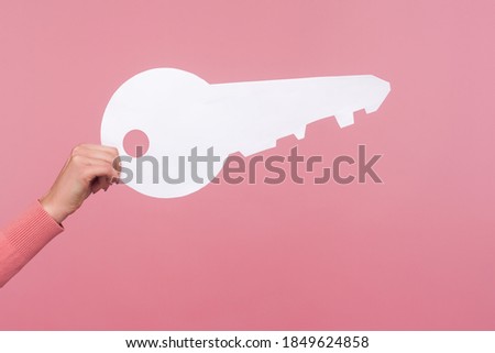 Closeup side view of female hand holding big white house key, real estate advertisement, house purchase, apartment rent. Indoor studio shot isolated on pink background