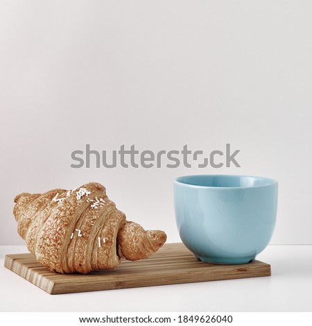 Croissant and a mug on a wooden stand, a vase and a pot with a plant on the books, white background. Eco-friendly materials in interior decor, minimalism. Copy space, mock up
