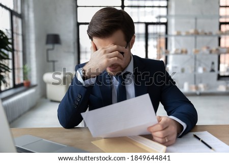 Frustrated 30s employee in formal wear holding paper dismissal notice, unhappy confused young businessman feeling stressed about bad news in letter, company bankruptcy or financial problems. Royalty-Free Stock Photo #1849644841