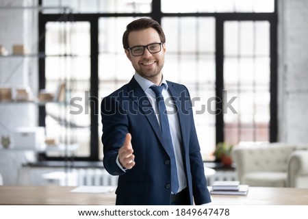 Happy young businessman in glasses looking at camera, reaching out hand making welcoming gesture or ready handshaking with partner or colleague, smiling banker proposing good deal to client. Royalty-Free Stock Photo #1849647478