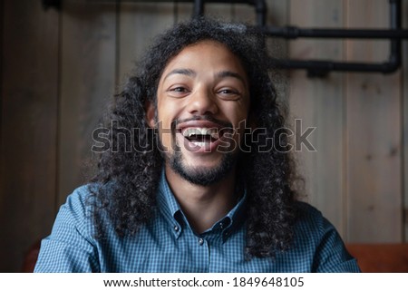 In a good mood. Profile picture of joyful laughing young mixed race male looking at camera, portrait of millennial biracial student sitting in cafe having fun with friends online using gadget webcam
