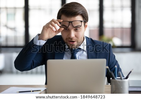 Surprised lucky 30s male ceo manager employee in formal wear can't believe his eyes, looking at laptop screen, feeling excited by unexpected news, salary increase notification or job promotion. Royalty-Free Stock Photo #1849648723