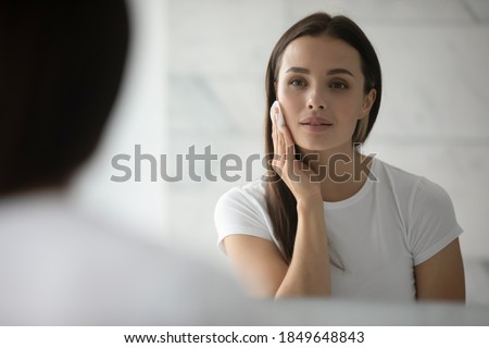 Beauty needs care. Pretty young lady doing daily morning skincare procedures, cleansing face skin with natural lotion tonic using cotton disc sponge pad, removing makeup by micellar water at evening Royalty-Free Stock Photo #1849648843
