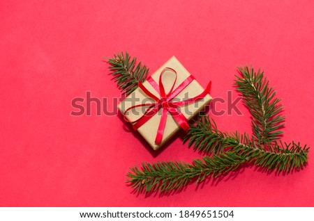 Natural spruce tree branch with a fir cone and Christmas decorations on a red background. Merry christmas and New Year. A minimalist composition, celebration and giving gifts. Copy space, flat lay.