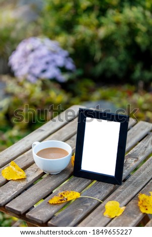 Cup of coffee and frame for picture on a table in garden
