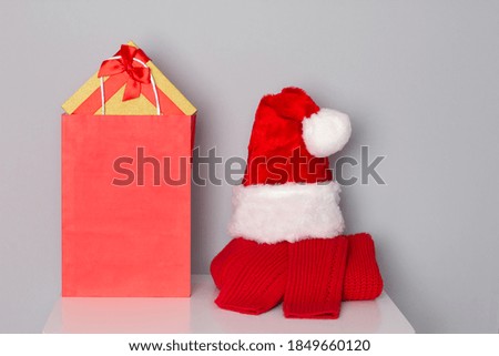 Santa hat, red sweater and paper shopping bag filled with Christmas gifts on white table. Christmas preparations concept