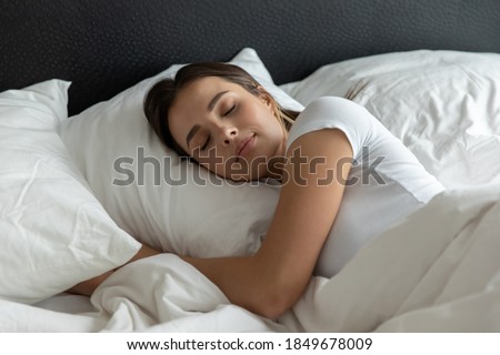 Sweet dreams. Relaxed young female sleeping in large cozy bed at home or in hotel suite room on clean white bedclothing hugging soft pillow covered with warm blanket dreaming resting having pleasure Royalty-Free Stock Photo #1849678009
