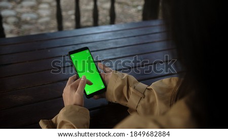Close up of a woman's hand holding a mobile telephone with a vertical green screen in park chroma key smart phone technology cell phone, technology and lifestyle concept