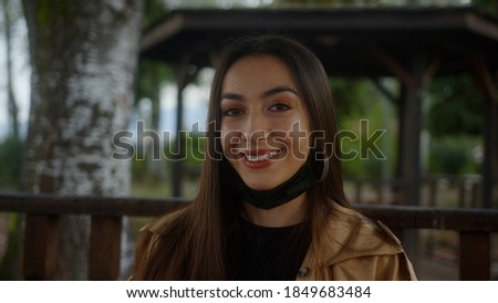 Charming beautiful woman wearing black mask, sitting on a bench during pandemic period and she is taking off her mask and breathing and smiling while looking at camera, lifestyle and