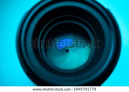 Close up camera lens reflection  under light blue neon light with colorful neon highlights against light blue background