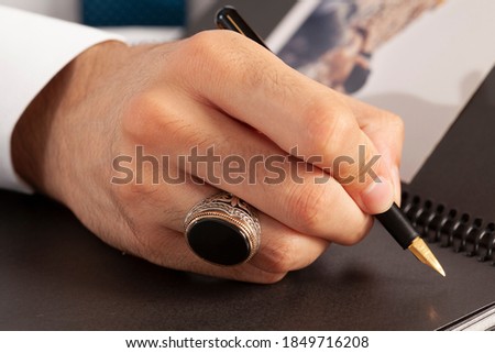 Man writing with a black silver ring on his finger.