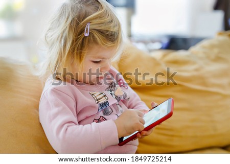Cute little toddler girl playing with smartphone at home. Healthy baby touching phone with fingers, looking cartoons and having fun with educational games . Early development concept