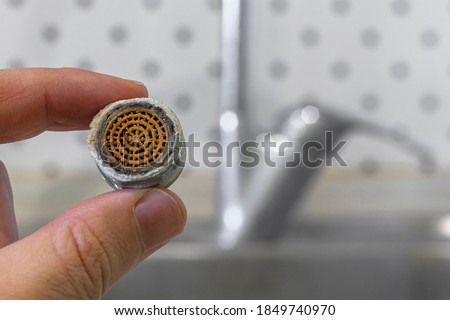 Old tap aerator in hand close-up. Selective focus. Blurred kitchen sink faucet on background. Royalty-Free Stock Photo #1849740970